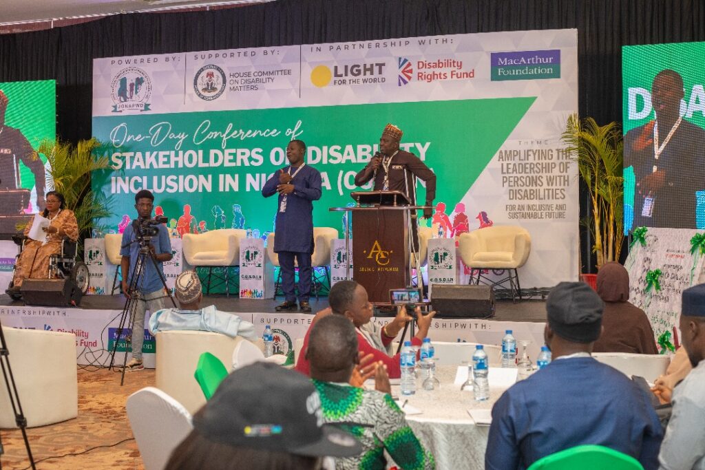 Prominently on the stage is the National President of JONAPWD and a sign language interpreter by his left side. Listening to him is a cross-session of participants at the 2024 COSDIN