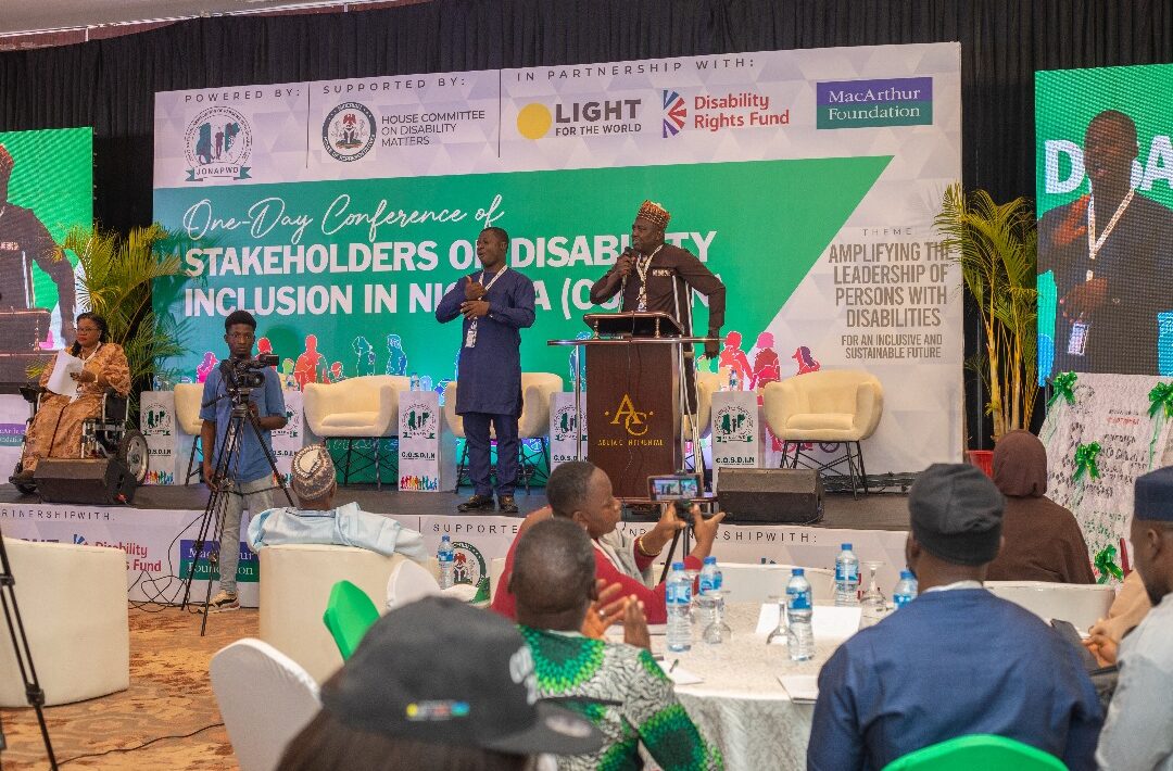 Prominently on the stage is the National President of JONAPWD and a sign language interpreter by his left side. Listening to him is a cross-session of participants at the 2024 COSDIN
